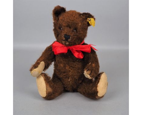 Steiff Teddybär, Nr. 5325.02, um 1962Teddybär von Steiff mit Knopf im Ohr. Sitzender brauner Teddy mit einer roten Schleife u