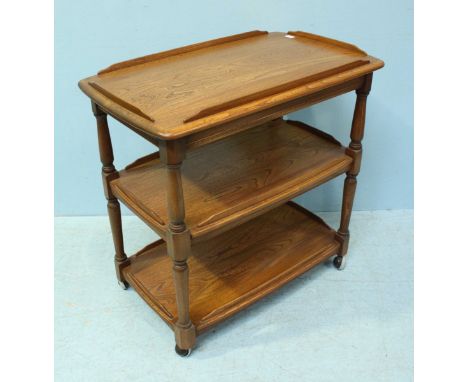An Ercol light elm three-tier trolley, raised on turned supports to castors. 80cm.