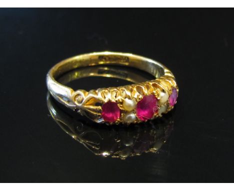 An 18ct gold ruby and seed pearl ring with scroll shoulders, (one pearl split), size M, 2.6g