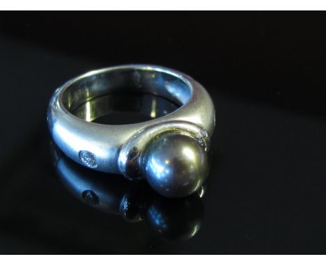 A white gold cultured pearl and diamond ring, the centre grey cultured pearl with frosted shoulders set with single diamonds 