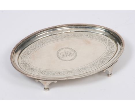 A George III silver teapot stand, having bright cut decoration and central monogram, raised on four scrolled feet, London 179