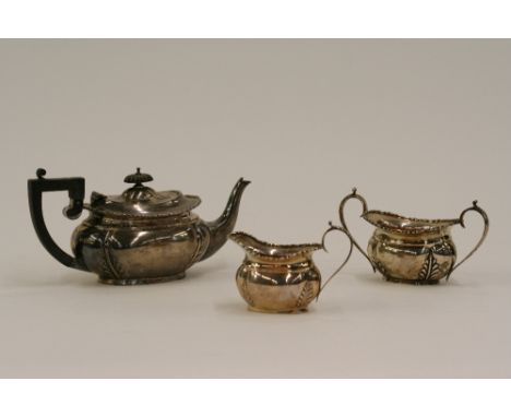 A George V three piece silver bachelors teaset, of lobed form with foliate decoration, the teapot with black wood handle and 