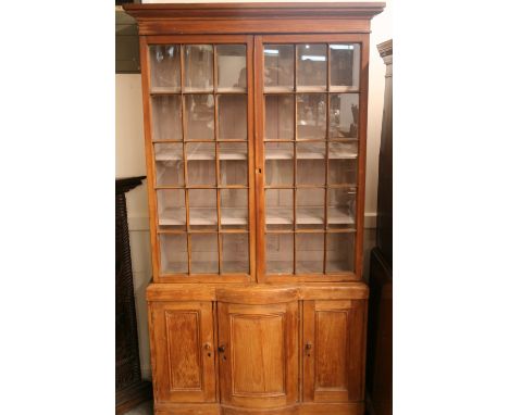 An early 19th Century stripped pine bookcase, the upper shelves enclosed by glazed panelled doors above a bow fronted base, f