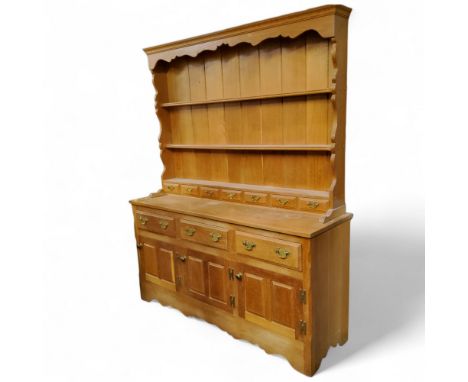 A modern limed oak kitchen dresser, oversailing ogee cornice above shaped sides holding g three shelves above seven small dra