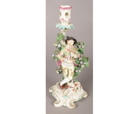 An 18th century Derby porcelain figural candlestick, modelled as a bagpipe player and dog, with bocage. 28cm.  Restoration to
