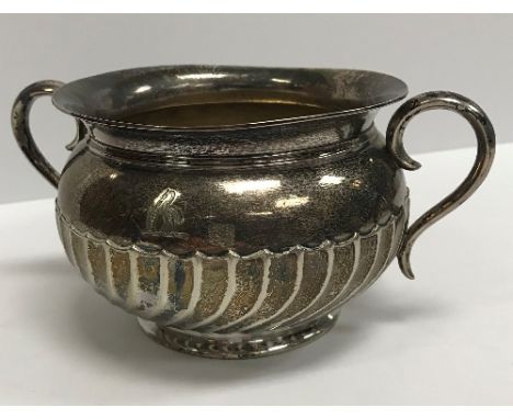 A late Victorian silver sugar basin with flared rim and wrythen embossed decoration flanked by scrollwork handles, raised on 