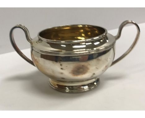 A George V silver sugar basin with gilt-washed interior flanked by open handles, raised on a circular foot (by Elkington &amp