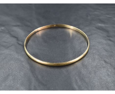 A yellow metal bangle, marked 9ct of rounded design having line engraving, approximately 20cm inner circumference, 9g. Uneven