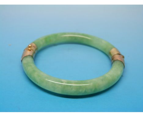 A jade or jadeite bangle with hinged yellow metal mounts and clasp