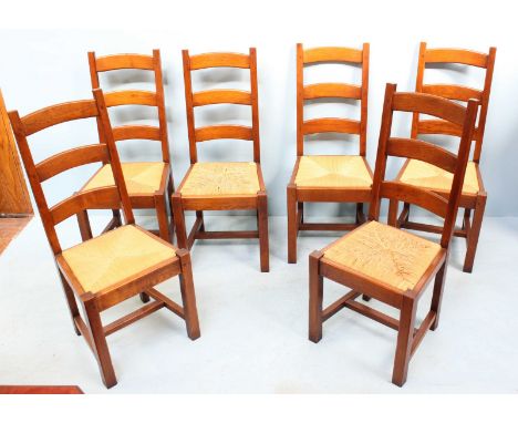 A set of six oak ladder-back chairs with rush woven drop in seats and raised on square supports.