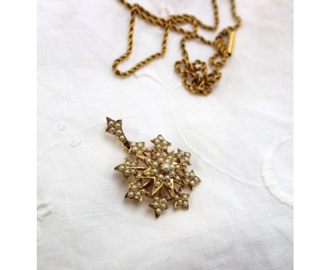 A yellow metal pearl set pendant of star shape on a yellow metal chain