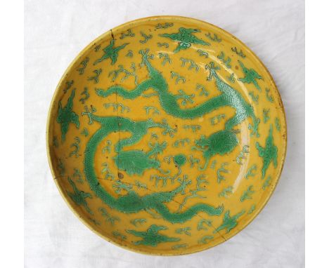 A Chinese porcelain saucer dish in green and yellow enamels decorated with dragons chasing a pearl amongst clouds, Kangxi six