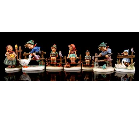 7 Goebel Hummel earthenware figurines of boys and girls sitting and standing on and near a fence, largest 13.5 cm high