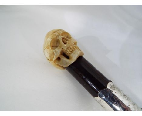 A walking stick with a bone carved skull and a white metal collar. Estimate £30 - £40