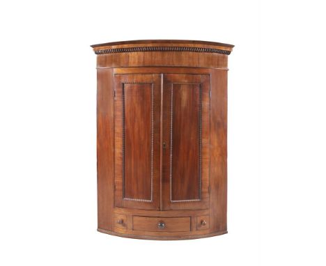 A GEORGE III MAHOGANY BOWFRONT CORNER WALL CUPBOARD, having twin single panel doors with egg and dart decoration, above three