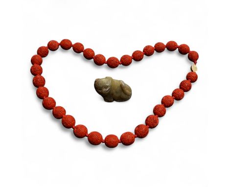 A Chinese red lacquered bead necklace and a bowenite jade figure of a cat