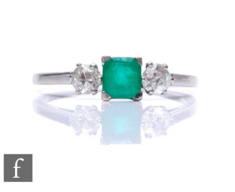 A mid 20th Century platinum emerald and diamond three stone ring, central square cut emerald flanked by an old cut diamond to