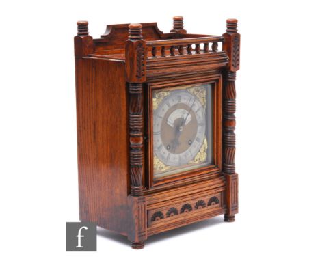 A late 19th Century oak bracket clock carved in the Aesthetic taste, with spindle gallery over pilaster supports either side 