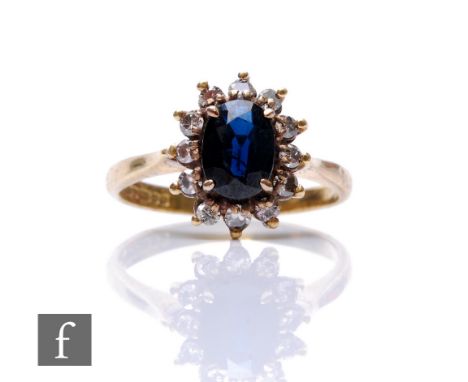 An 18ct hallmarked sapphire and diamond cluster ring, central oval sapphire, length 8mm, within a border of twelve claw set d