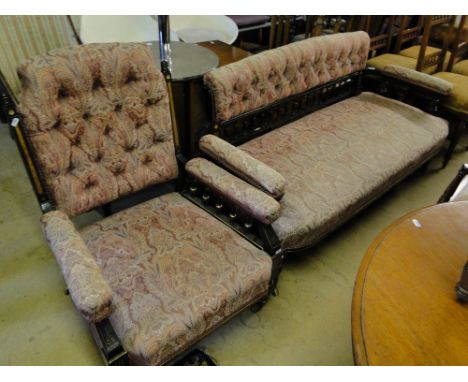 A Victorian ebonised bow arm parlour sofa with button back upholstery and a matching armchair with gilded decoration.