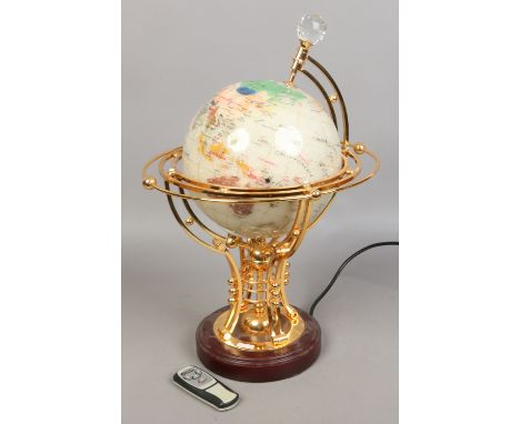 An electronic rotating light up hardstone globe with remote raised on brass stand.