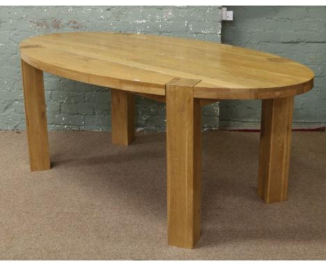An oval light oak dining table raised on square cut legs.