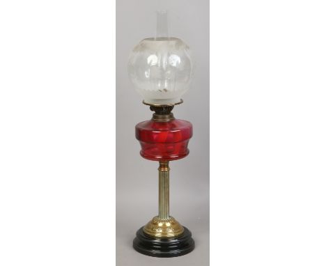 A brass column oil lamp with ruby glass font and frosted glass shade.