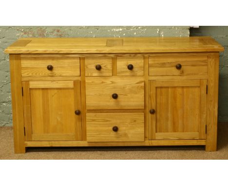 A light oak sideboard of six drawers flanked by a cupboard raised on heavy square cut leg.