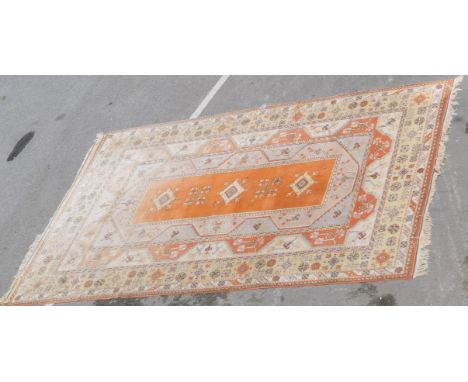 Turkish woollen carpet, having a central orange field with lozenge shaped medallions, within wide terracotta and orange borde
