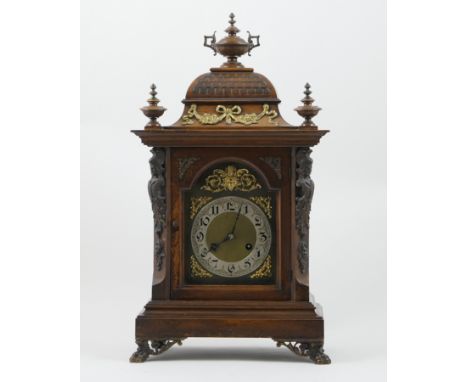 German walnut cased mantel clock, architectural case with domed top surmounted with urn finials, over two cast brass caryatid