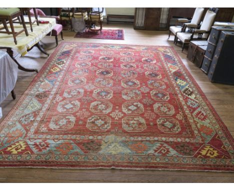 An Afghan carpet, the four rows of eight guls on a red field within a serrated border 412cm x 311cm