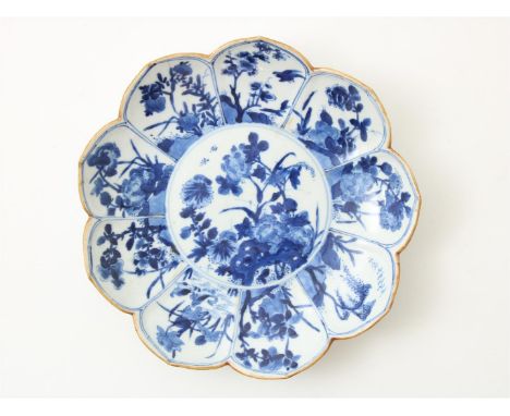 Lotusbladvormig blauw-wit porseleinen bord afgezet met bruine lip, met centraal decor van bloeiende heester op rots, waaromhe