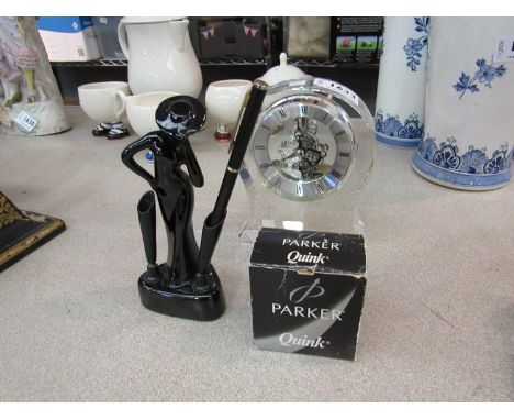 An Art Deco style ceramic pen holder in the form of a lady, Parker Quink ink bottle and a skeleton form desk/mantel clock