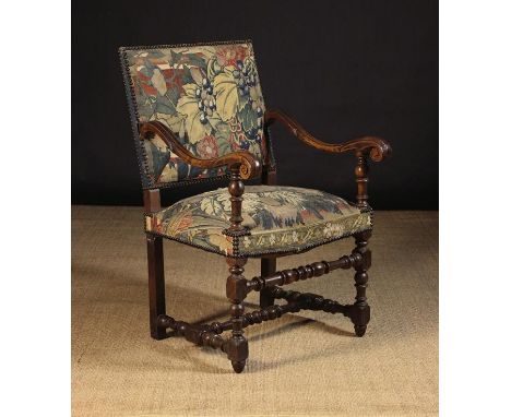 A 17th Century Carved Walnut & Tapestry Armchair. The rectangular slung back and upholstered seat covered in foliate tapestry