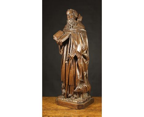 A Flemish Oak Carving of Saint Anthony, Circa 1500. The abbot depicted with curly hair and beard wearing a cowled flowing clo