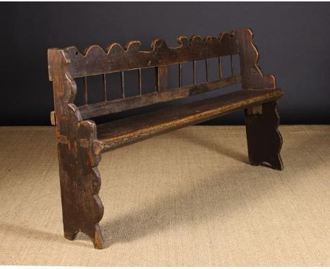 An 18th Century Provincial Elm Bench having a wavy cut back rail above a row of stick spindles, and a long plank seat mortice