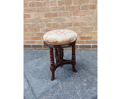 A VICTORIAN CIRCULAR ADJUSTABLE MUSIC STOOL with upholstered stuff over seat and raised on three turned supports with outswep