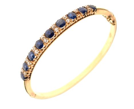 Edwardian sapphire and diamond hinged bangle, in unmarked gold, the nine oval cut graduated sapphires with pairs of old cut d