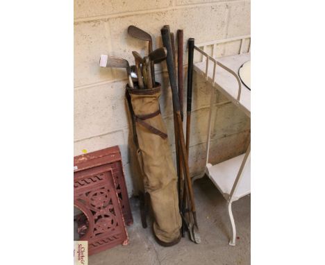 A vintage canvas and leather golf bag and a quantity of vintage hickory shafted golf clubs