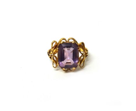 A gold ring, claw set with a cut cornered rectangular step cut amethyst, between pierced shoulders, in an Art Nouveau design,