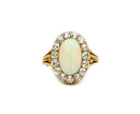 A gold, opal and diamond set oval cluster ring, mounted with the oval opal within a surround of cushion shaped diamonds, betw