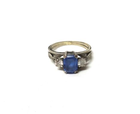 A tanzanite and diamond set three stone ring, claw set with the cut cornered rectangular step cut tanzanite at the centre, be