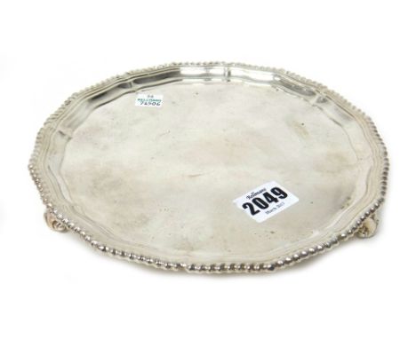 A silver salver, of shaped circular form, in the Chippendale style, decorated with a gadrooned rim and raised on three scroll