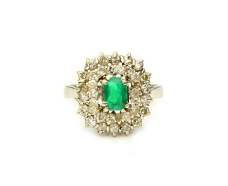 A white gold, emerald and diamond cluster ring, claw set with the cut cornered rectangular step cut emerald at the centre, in