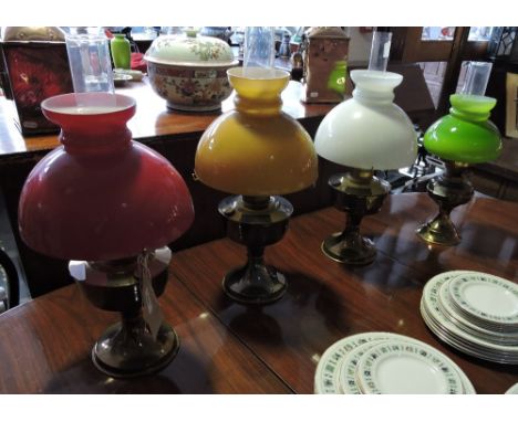 Four vintage brass oil lamps with coloured glass shades