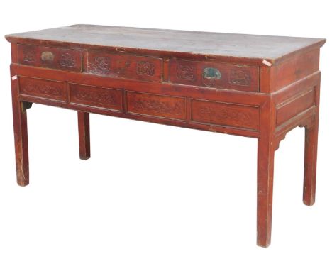 A Chinese red stained hardwood side table, with three carved frieze drawers, above a carved four panel frieze, raised on squa