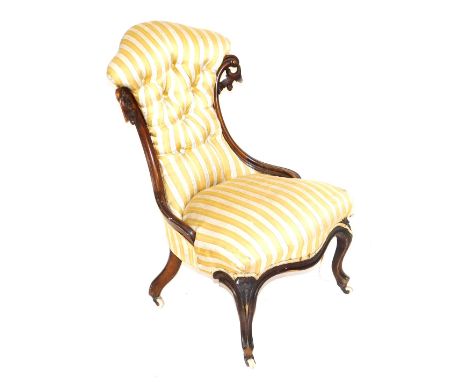 A Victorian mahogany nursing chair, with foliate carving, button back and overstuffed yellow and white striped fabric, raised