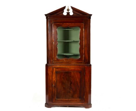 An early 19th Century mahogany corner cupboard in two sections with swan neck pediment, the top fitted shaped shelves enclose