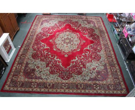 A large machine made Persian design carpet, crimson ground with central floral motif, having scrolling floral corners &amp; d