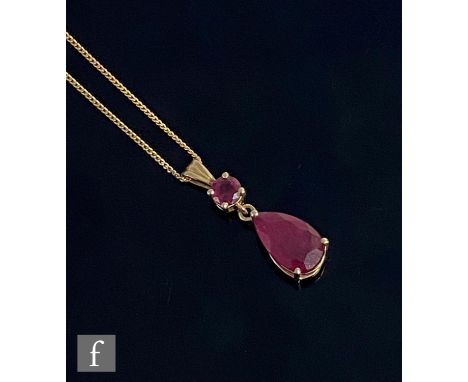 A modern 9ct ruby two stone pendant, claw set pear shaped stone length 14mm, below a round cut example, suspended from a 9ct 